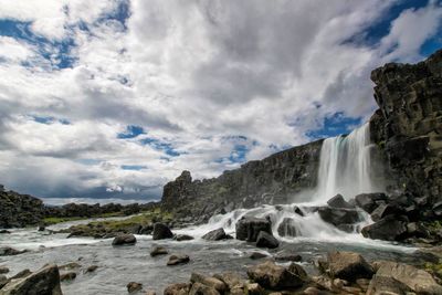 Scenic view of oxararfoss waterfall against cloudy sky
