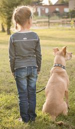 Rear view of girl and dog on grassy field