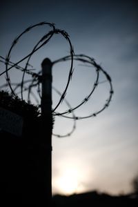 Close-up of silhouette barbed wire against sky during sunset