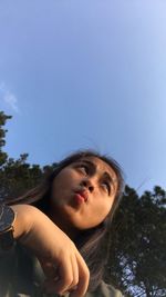 Low angle view of young woman making face against blue sky