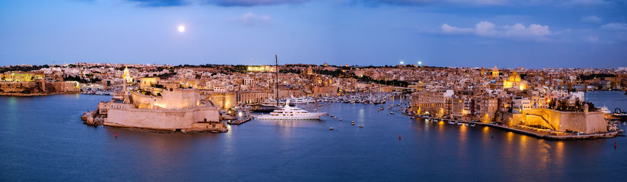 Panoramic view of sea and buildings against sky at dusk