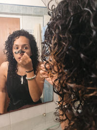 Woman peeling off black facial mask of her face in the bathroom.