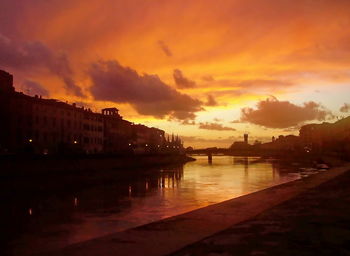 Silhouette buildings by river against orange sky