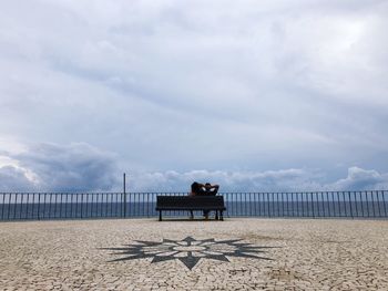 Rear view of people sitting on bench on beach