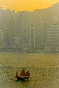 Boat in river by buildings in city against sky during sunset