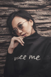 Portrait of young woman wearing sunglasses against wall