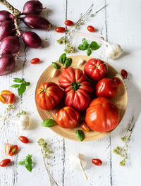 Tomatoes on the plate and white wooden background with oregano, basil leaves, garlic and onion