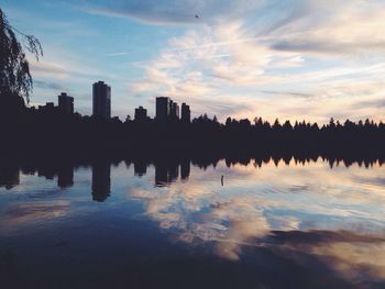 Scenic view of lake by silhouette buildings against sky at sunset