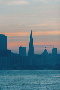 Sea by buildings against sky during sunset