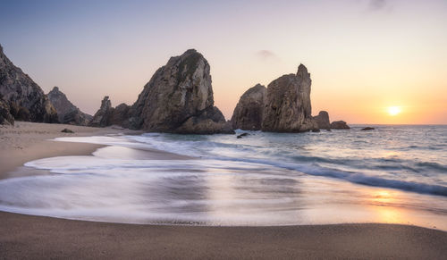 Rocks at beach against sky during sunset