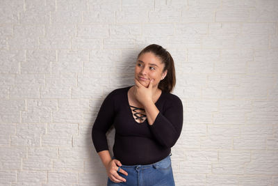 Portrait of a smiling young woman standing against wall