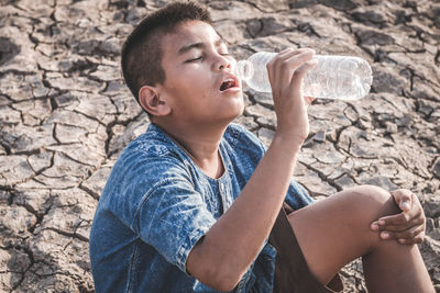 High angle view of boy drinking water while sitting on barren field