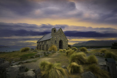 Old temple by building against sky during sunset