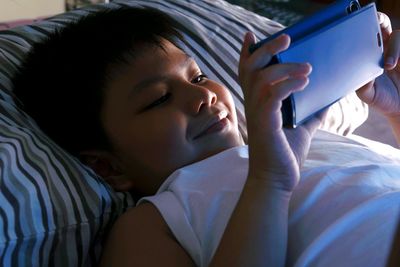 Close-up of boy using smart phone while lying down on bed at home