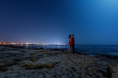 Couple kissing while standing at beach against clear blue sky
