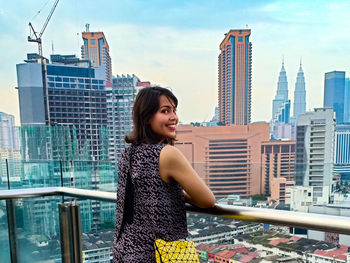 Smiling young woman standing against modern buildings in city