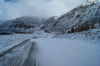 Snow covered road by mountain against sky