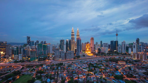 Petronas and kuala lumpur towers amidst illuminated city against sky at dusk