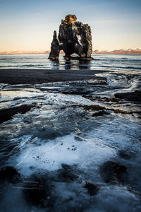 Rock formation on beach against sky during sunset