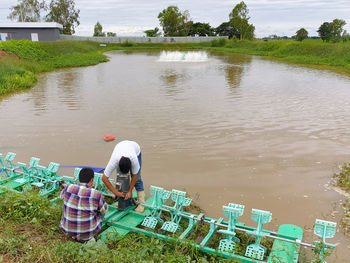 Rear view of people sitting by lake against sky