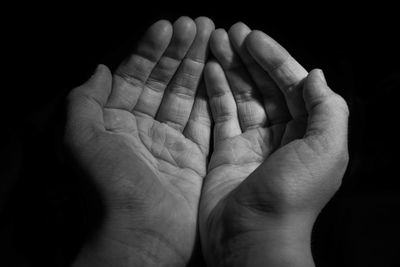 Close-up of human hand praying against black background