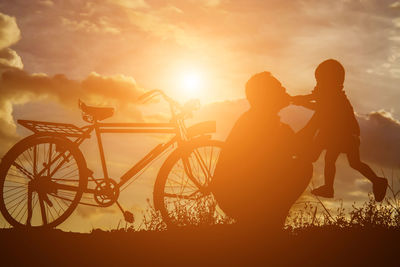 Silhouette people with bicycle against sky during sunset