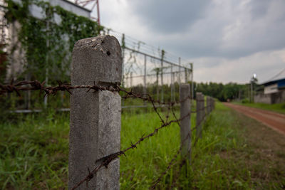 Barbed wire fence on field against sky