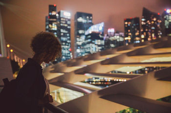 Woman standing at railing against illuminated city at night