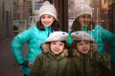 Portrait of cute smiling siblings wearing warm clothing by window in winter