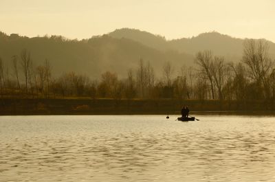 Silhouette man on boat in lake against clear sky