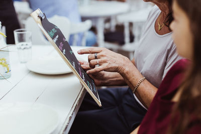 Midsection of woman holding menu while sitting with granddaughter in restaurant