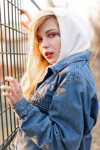 Portrait of beautiful young woman standing by fence