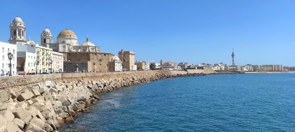 Buildings by sea against clear blue sky