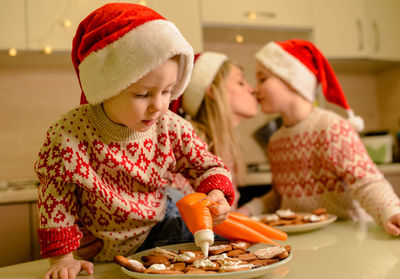 Mom and little sons are decorating homemade gingerbread xmas cookies