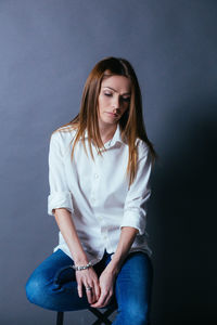 Thoughtful woman sitting against gray background