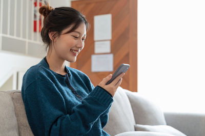 Young woman using mobile phone while sitting at home