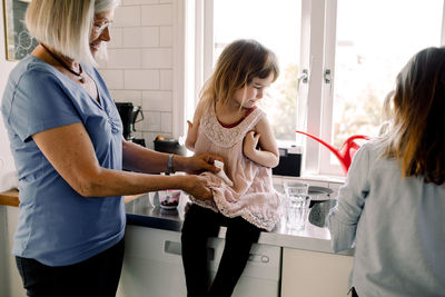 Grandmother cleaning granddaughter's dress by girl working at counter in kitchen