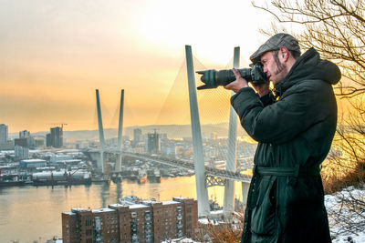 Man photographing cityscape against sky during sunset