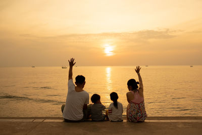 Rear view of people sitting at beach during sunset