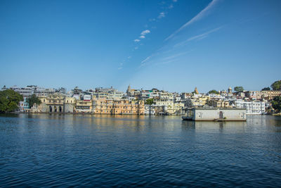 Buildings by river against blue sky