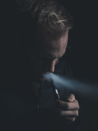 Close-up of young man smoking against black background