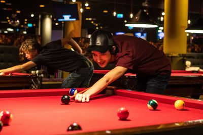 Confident teenage boys playing pool on illuminated red tables