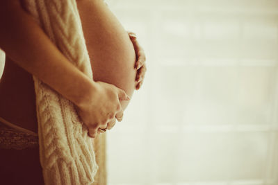 Midsection of pregnant woman standing at home