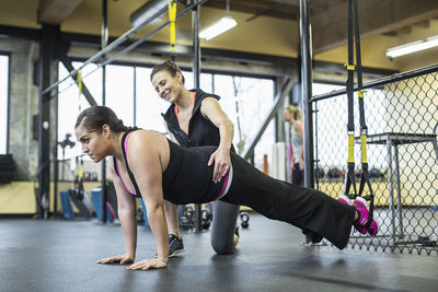 Instructor assisting woman in balancing on resistance band with legs ay gym