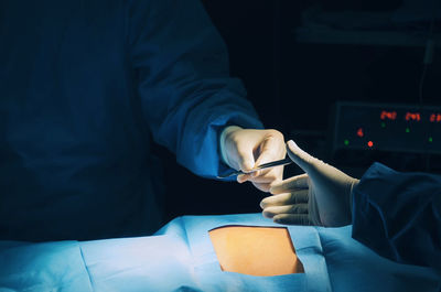 Cropped hand giving equipment to surgeon in darkroom