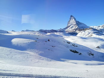 Scenic view of snow covered mountain against blue sky