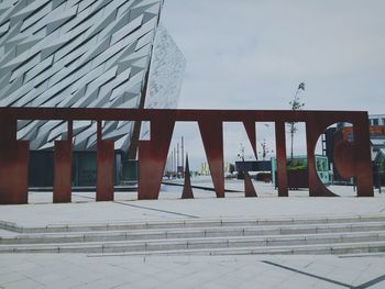 View of footpath by building against cloudy sky