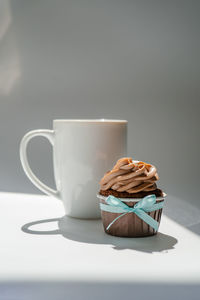 A cupcake or muffin stands next to a cup of coffee.