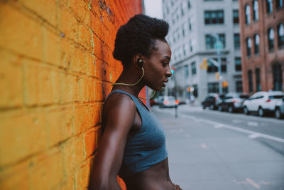 Side view of woman listening music while standing by wall