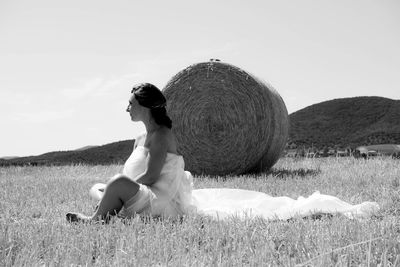 Woman sitting on field against sky